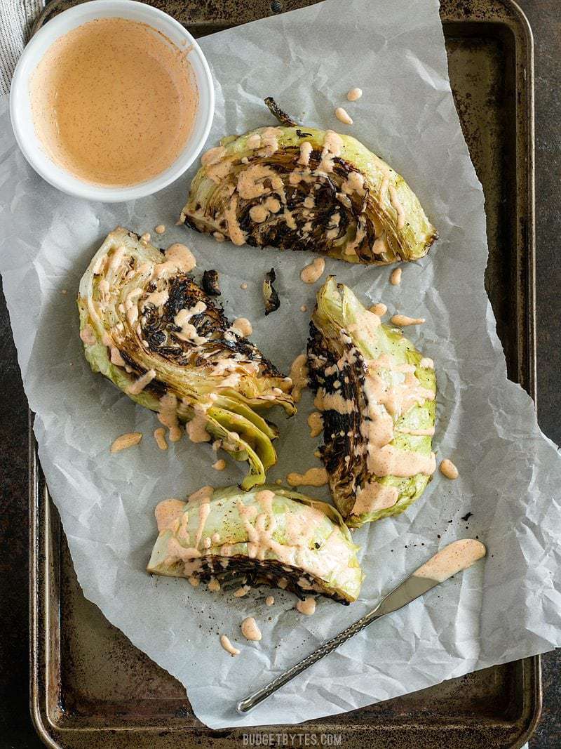 Blackened Cabbage wedges on a parchment lined baking sheet, drizzled with chipotle mayo
