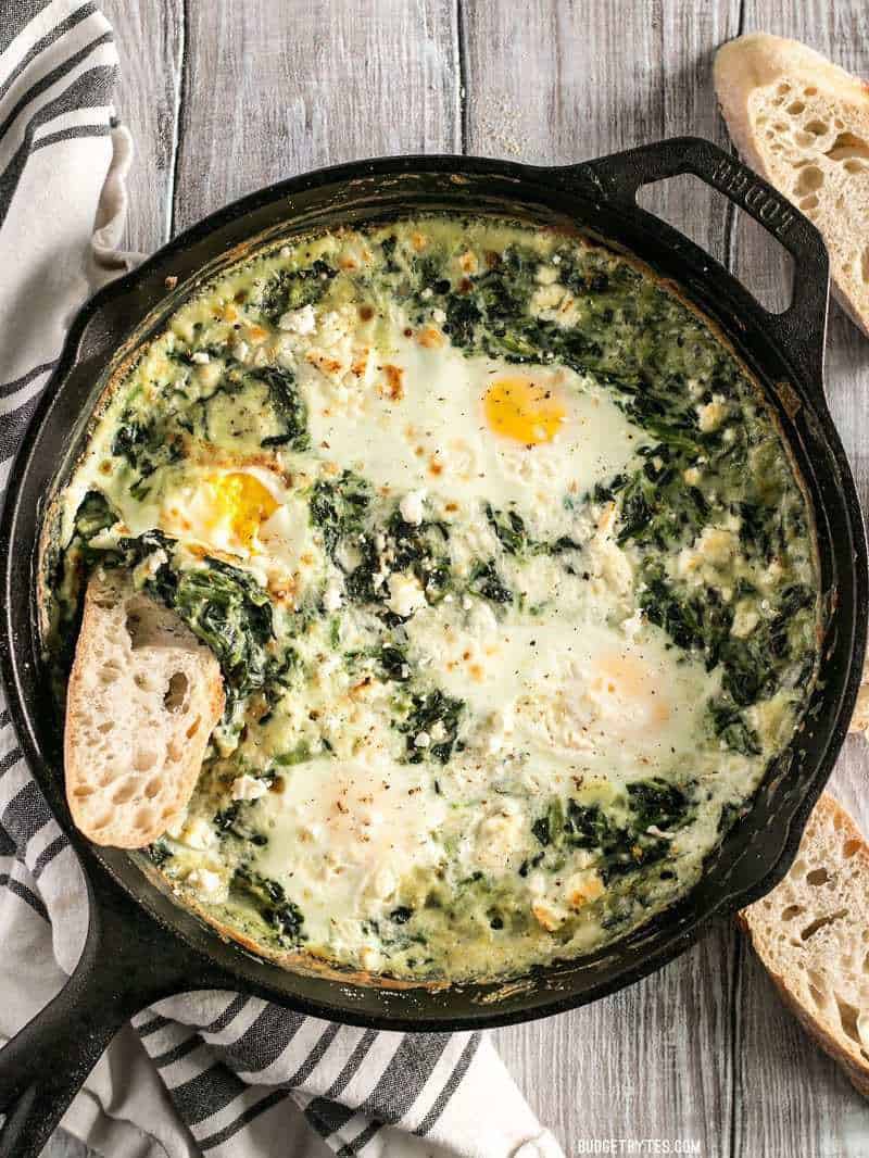 Overhead shot of a cast iron skillet full of Creamed Spinach Baked Eggs with slices of bread