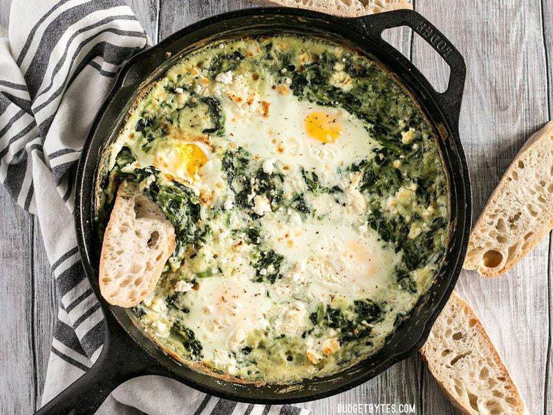 Overhead shot of Creamed Spinach Baked Eggs in a cast iron skillet with slices of bread