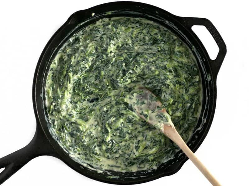 Creamy Spinach heated through in cast iron skillet with a wooden spoon