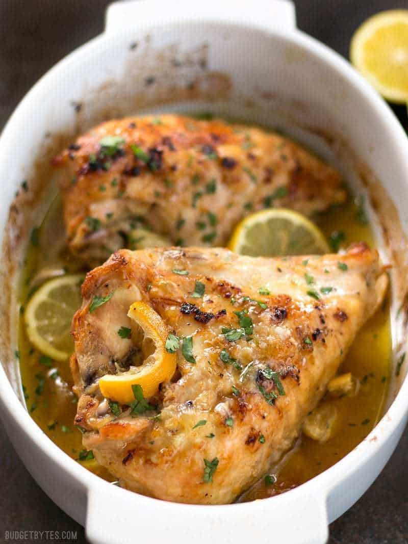 Front view of Lemon Garlic Roasted Chicken in a white casserole dish, garnished with lemon slices