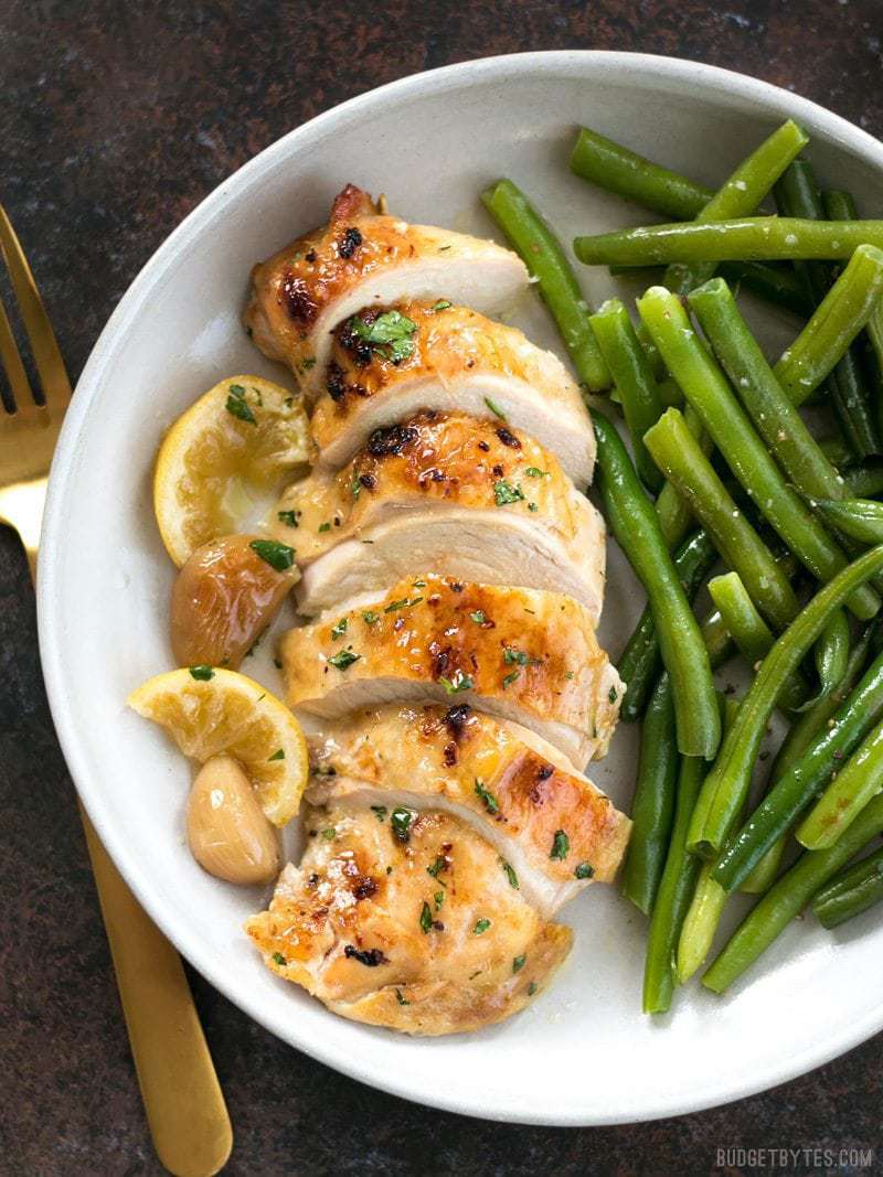 Sliced Lemon Garlic Roasted Chicken on a plate with cooked green beans