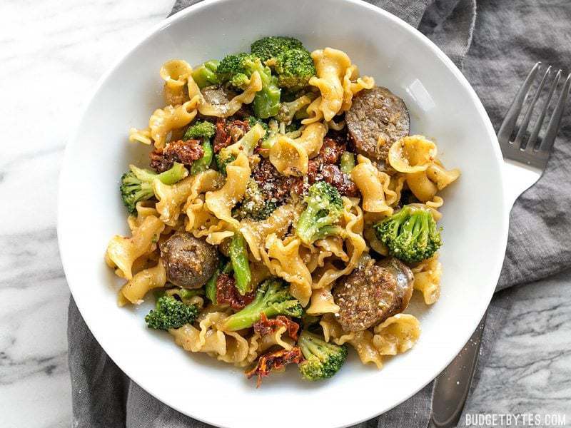 A bowl of One Pot Sausage and Sun Dried Tomato Pasta with a fork on the side