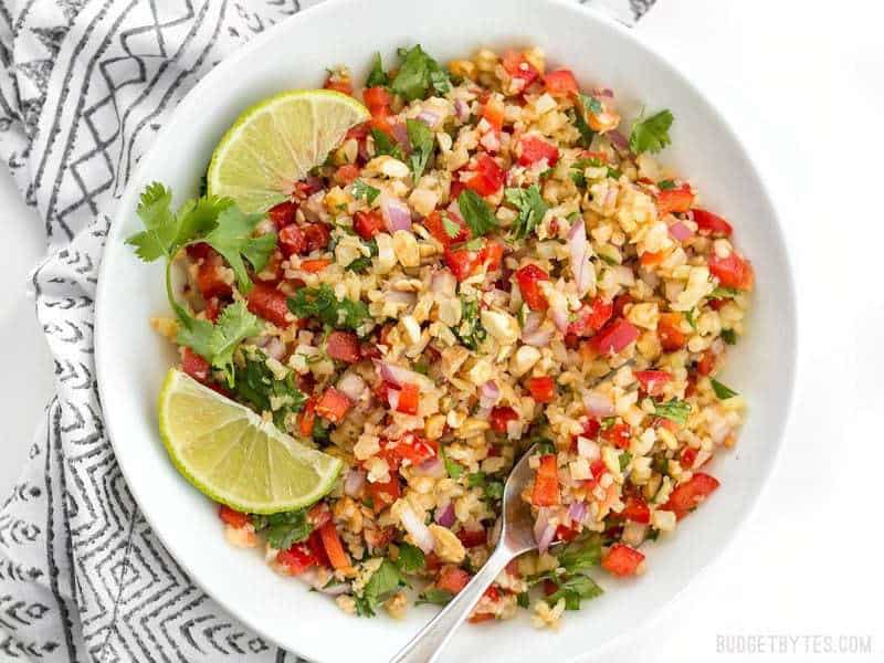 Overhead shot of Peanut Lime Cauliflower Salad in a bowl with lime wedges and cilantro