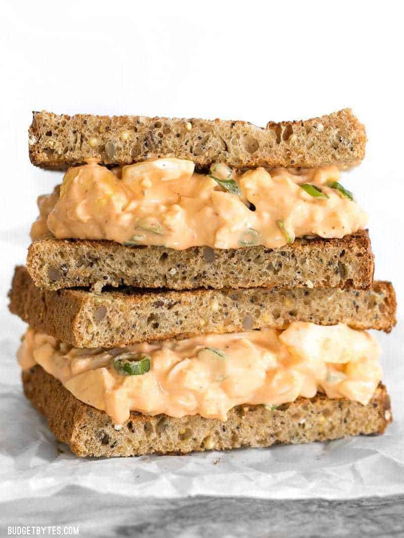 A Sriracha Egg Salad sandwich on wheat bread, two halves stacked, cut sides facing the camera