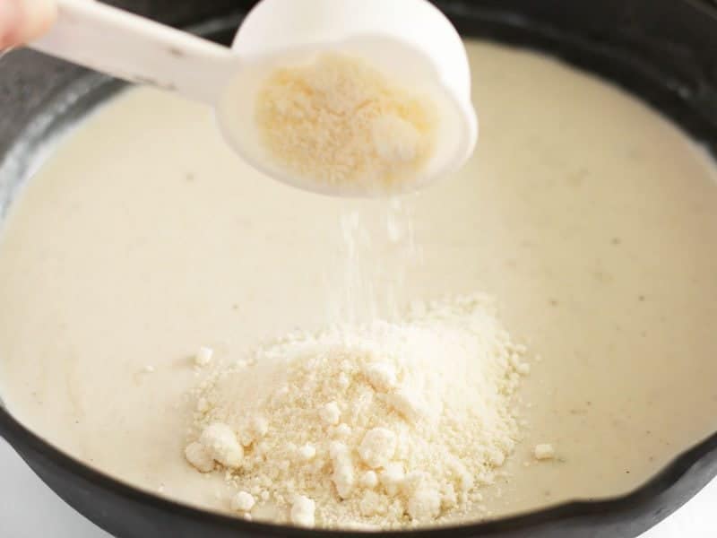 Grated Parmesan being added to the thickened white sauce