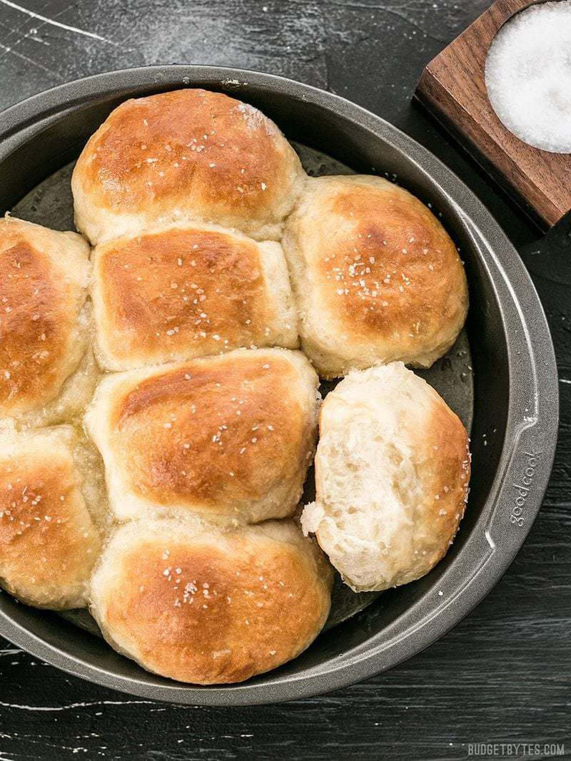 A round bread pan full of Buttermilk Pull-Apart Rolls with a dish of salt on the side