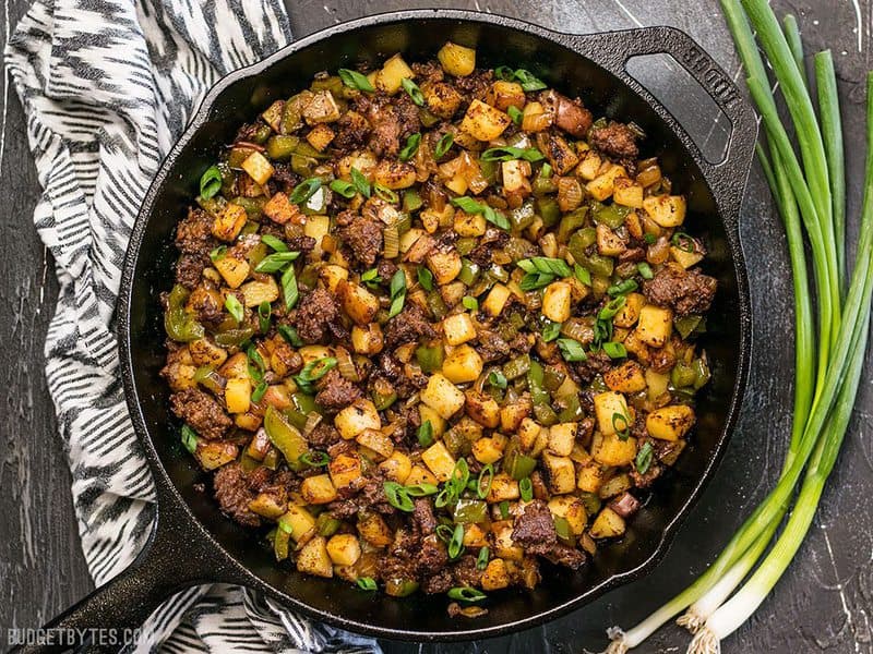 Finished Chorizo Breakfast Hash in a cast iron skillet next to green onion and a striped napkin