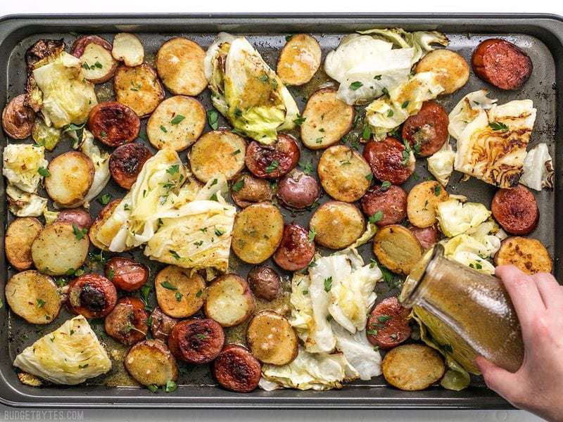 Mustard vinaigrette being drizzled over pan roasted kielbasa and cabbage