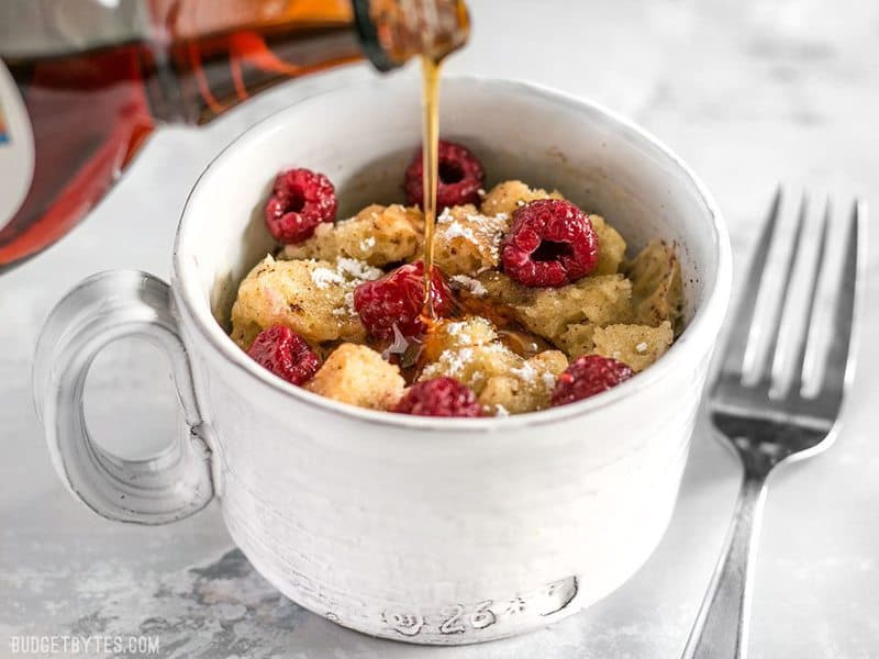 Maple syrup being poured into a Microwave French Toast Mug topped with raspberries
