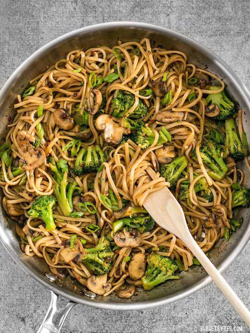 A large skillet full of Mushroom Broccoli Stir Fry Noodles, some wound around a wooden pasta fork