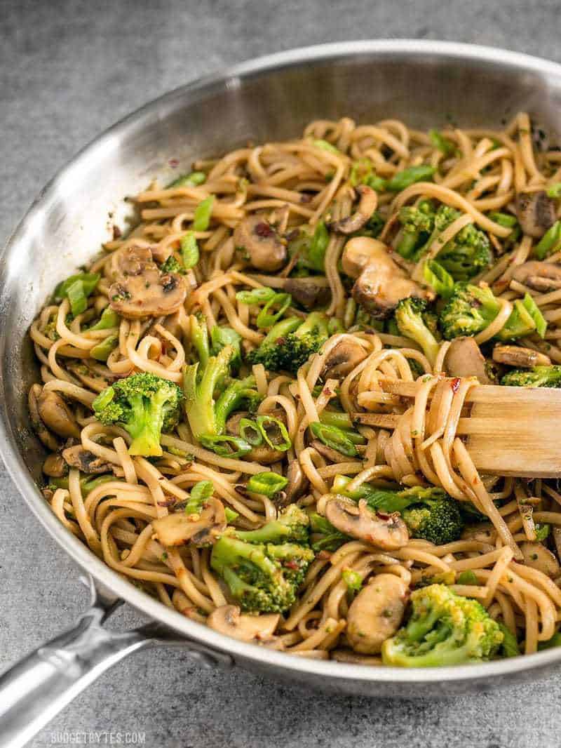 Side view of the skillet full of Mushroom Broccoli Stir Fry Noodles with a wooden pasta fork