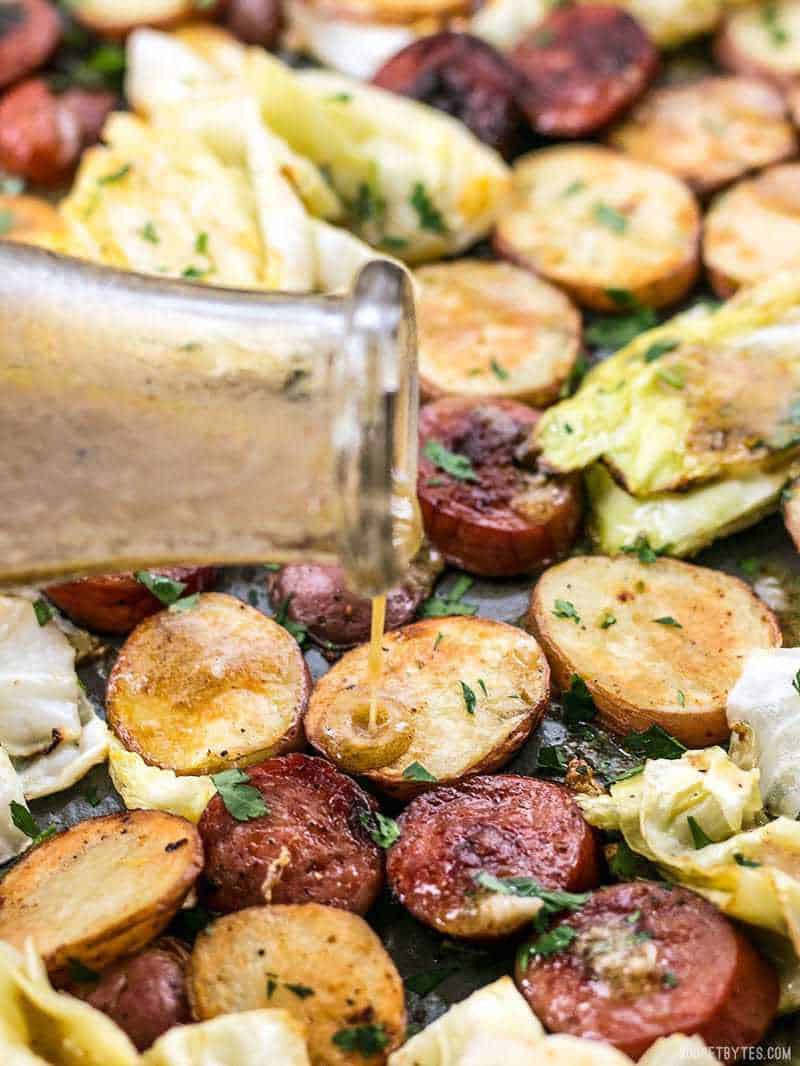 Vinaigrette being poured onto roasted kielbasa, potatoes, and cabbage