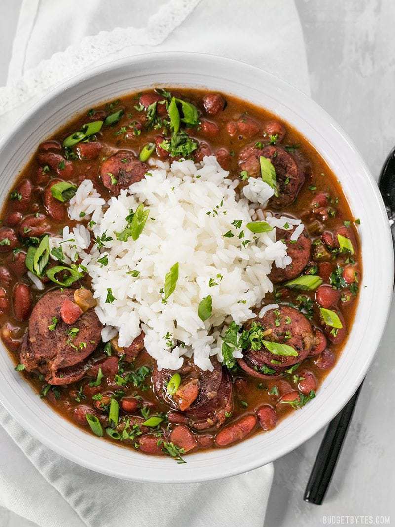 A big bowl of Pressure Cooker Red Beans with a scoop of white rice on top, garnished with parsley and green onions
