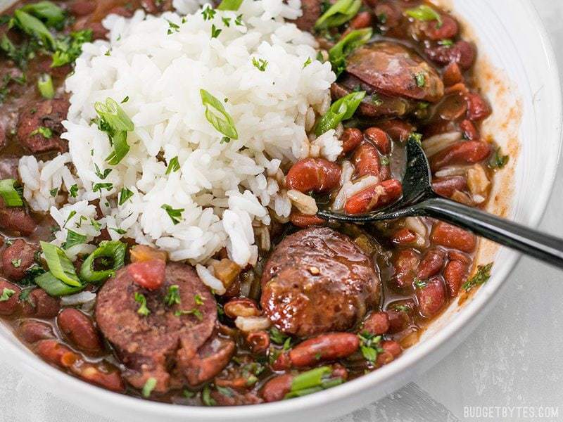Close up side view of a bowl of Pressure Cooker Red Beans with a black spoon lifting a scoop