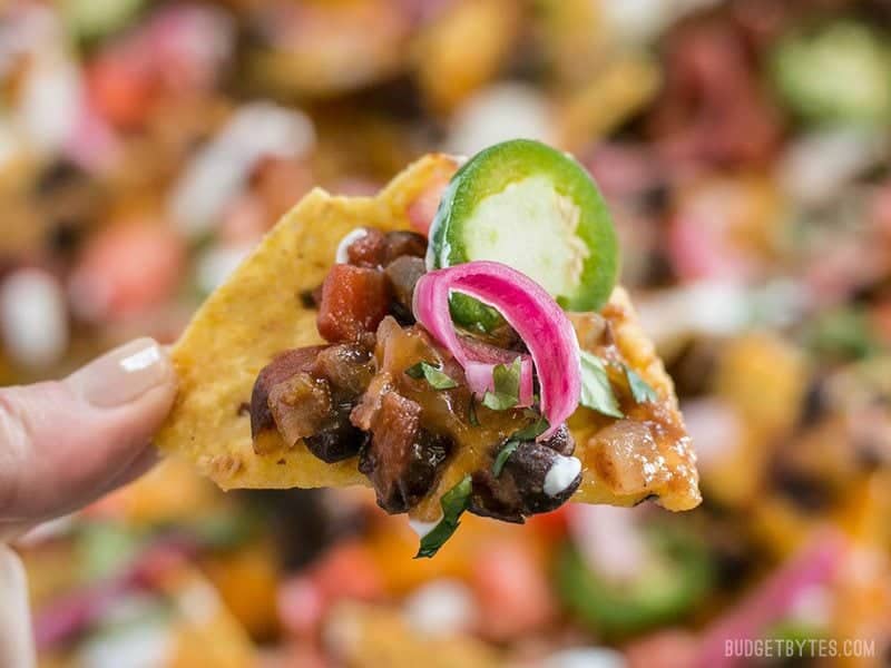 Close up of a Spicy Baked Black Bean Nacho with pickled onions and a slice of jalapeno