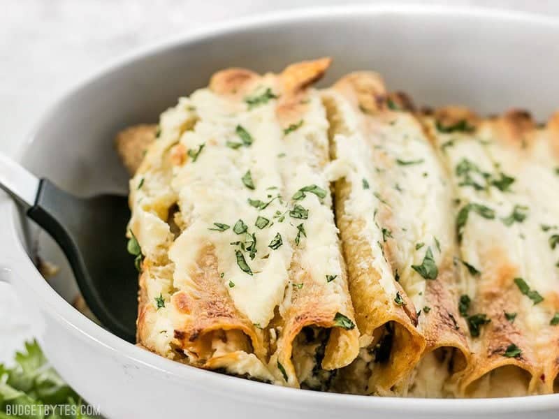 A spatula lifting Spinach White Bean Enchiladas out of the baking dish