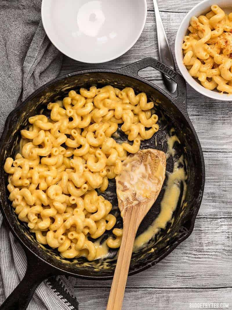 A skillet full of mac and cheese with a wooden spoon, next to two bowls