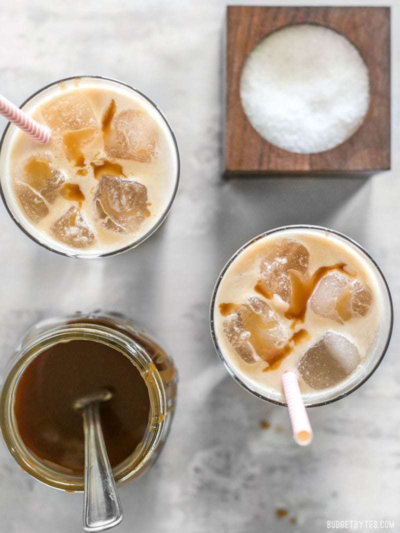 Two Homemade Salted Caramel Iced Coffees from above with caramel sauce and salt nearby 