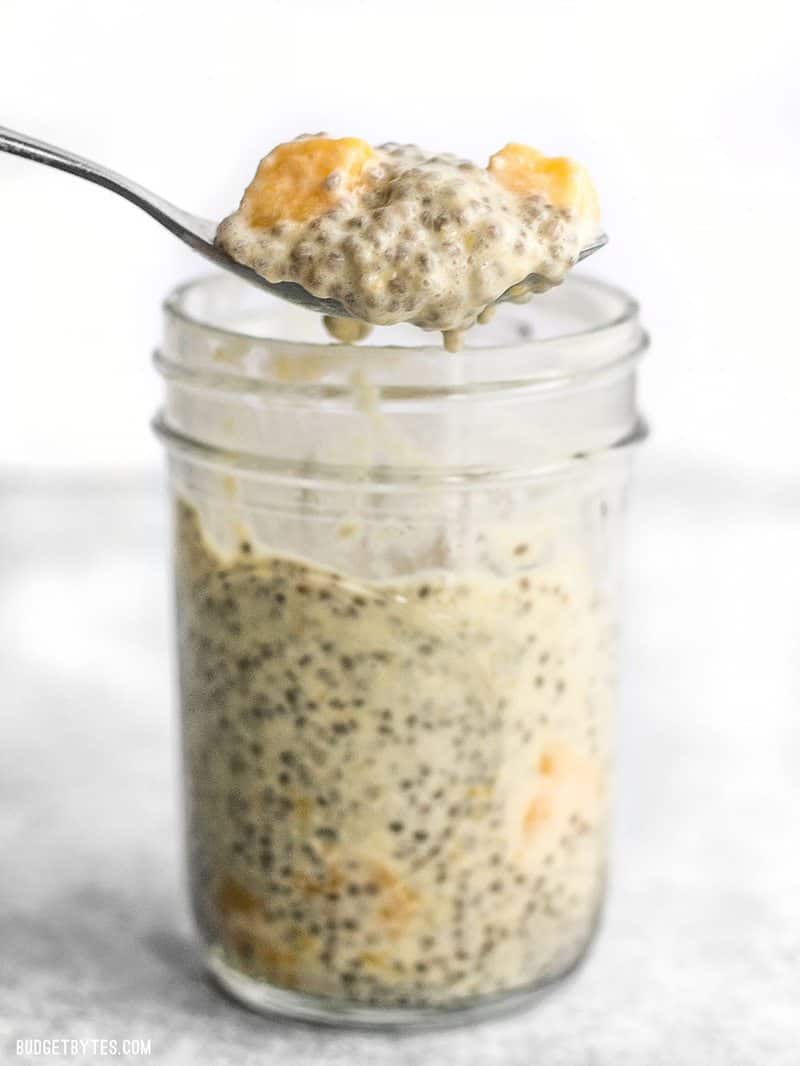 A jar full of Mango Coconut Chia Pudding with a spoon lifting a bite out the top