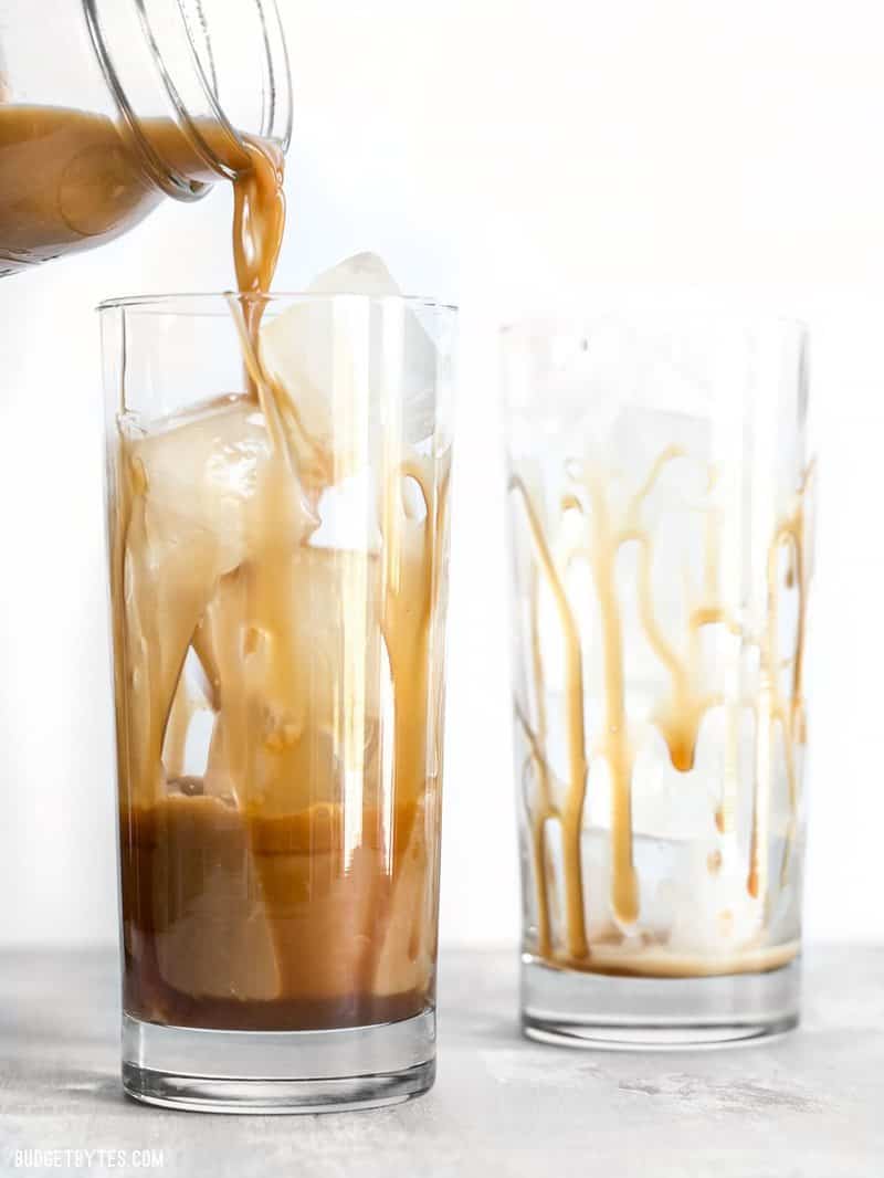 Iced coffee being poured into a glass coated with homemade caramel