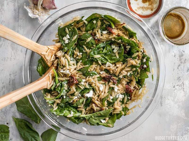 A glass bowl full of Spinach and Orzo Salad from above with a mason jar of dressing on the side
