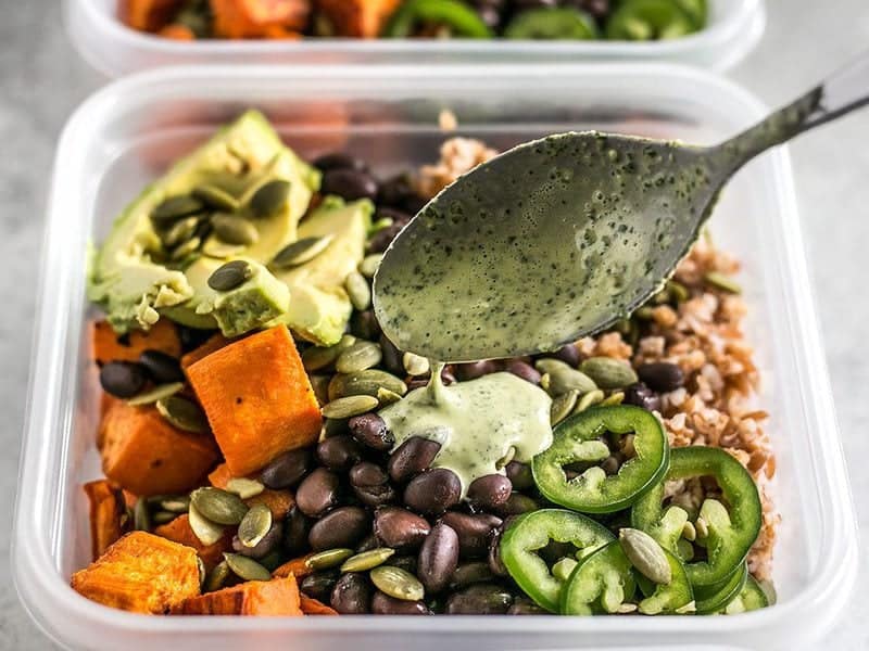 Green Tahini Sauce being drizzled over a meal prep container full of sweet potato grain bowls