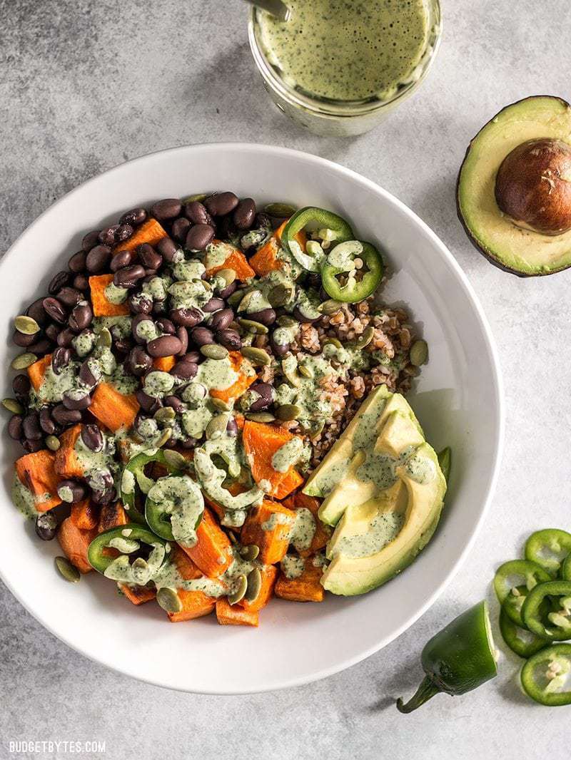 A prepared Sweet Potato Grain Bowl with a jar of green tahini dressing on the side