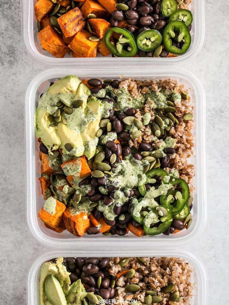 Four meal prep containers of Sweet Potato Grain Bowls with Green Tahini Sauce 