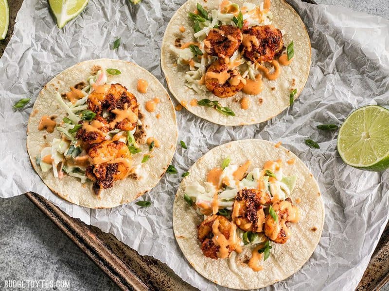 Drei geschwärzte Garnelen-Tacos auf Pergamentpapier mit Knoblauch-Limetten-Sauce beträufelt