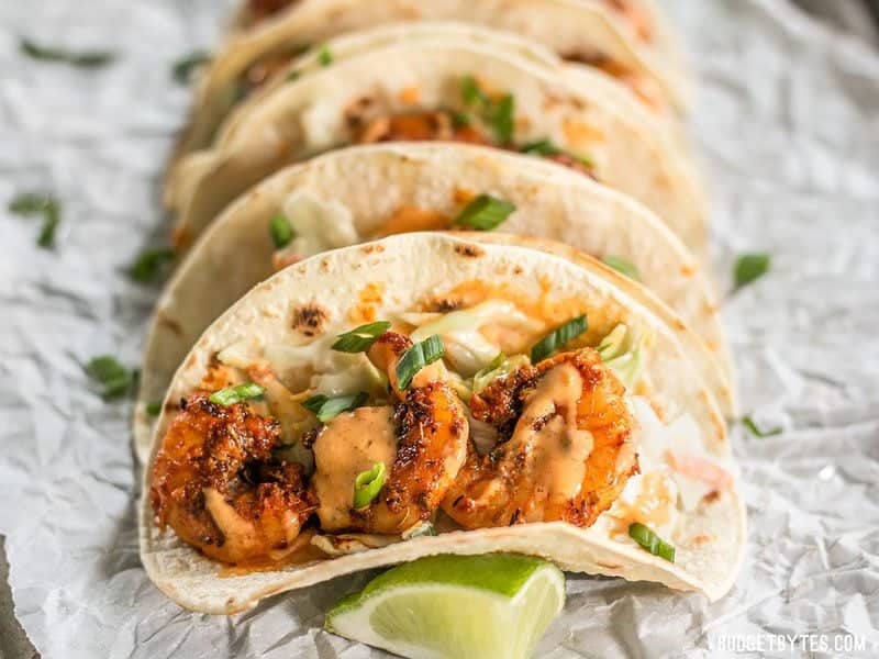 Vue de face rapprochée de Tacos aux crevettes noircies arrosés de sauce à l'ail et au citron vert.