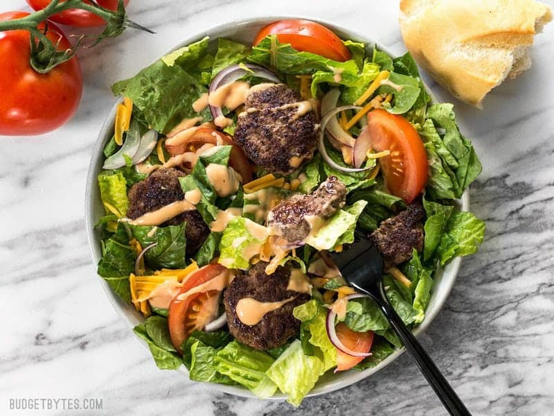 Cheeseburger salad from above with a fork taking a bite and bread on the side