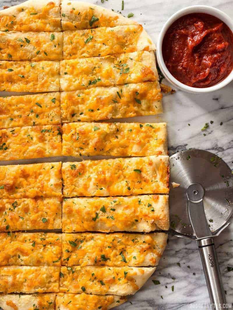 Sliced Homemade Cheesy Garlic Bread next to a ramekin full of pizza sauce