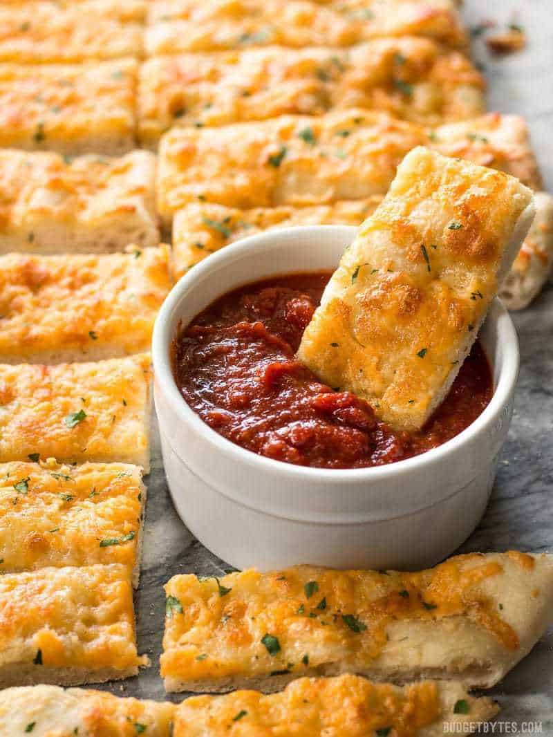 Homemade Cheesy Garlic Bread on a baking sheet, one piece being dunked into pizza sauce.