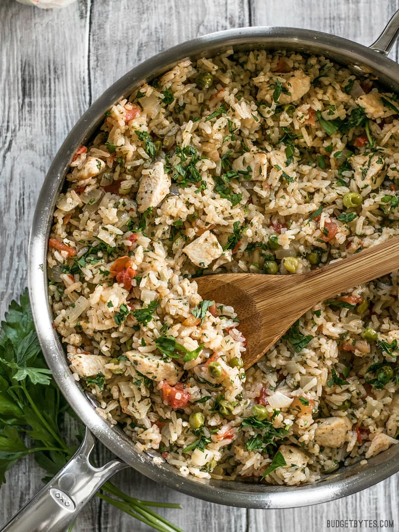 This Chimichurri Chicken and Rice is a bright and vibrant summer meal that cooks in just one pot to make dinner fast and easy. BudgetBytes.com Chimichurri Chicken and Rice in the skillet with a wooden spoon