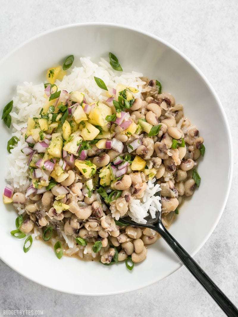 A white bowl full of Coconut Jerk Peas served over rice, topped with pineapple salsa.