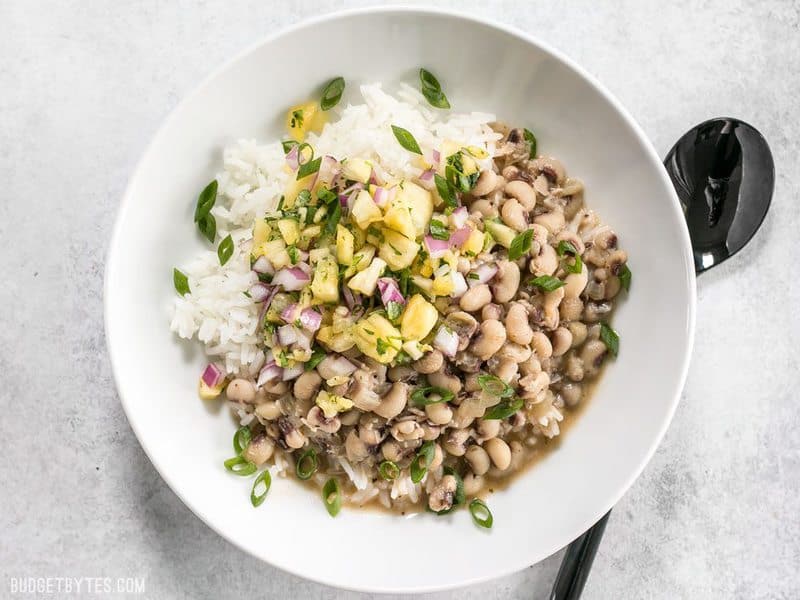 A bowl of Coconut Jerk Peas over rice, topped with pineapple salsa