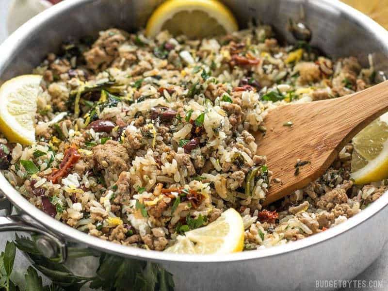 A wooden spatula stirring the Greek Turkey and Rice Skillet, with lemon wedges on the sides. 