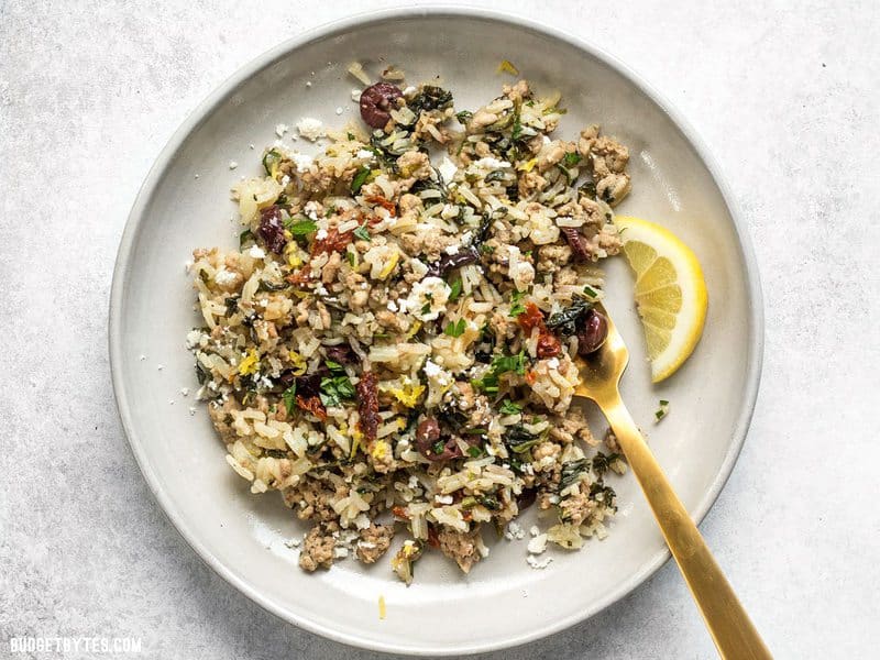 Greek Turkey and Rice Skillet on a stoneware plate with a lemon wedge and feta sprinkled over top.