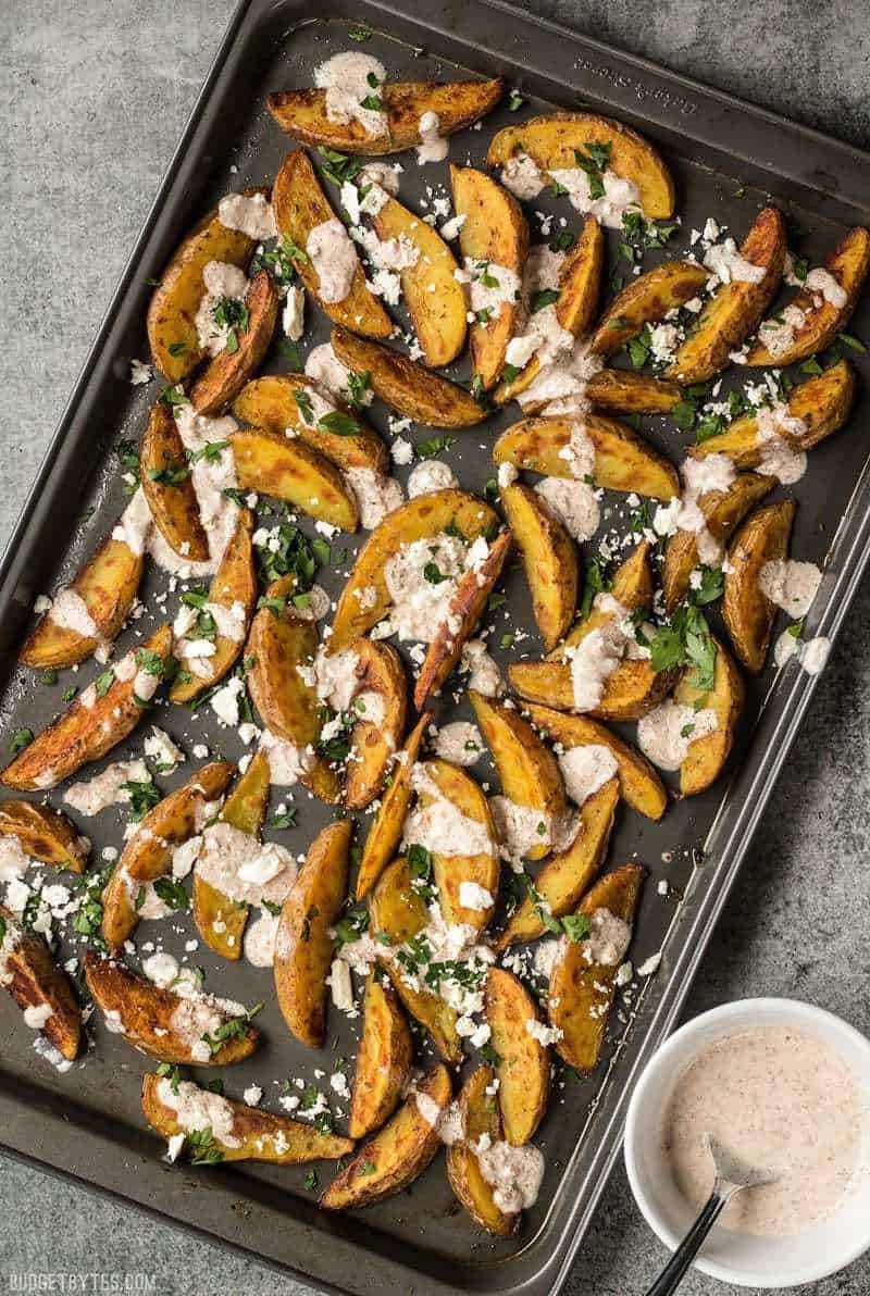 A sheet pan full of Roasted Potato Wedges with Shawarma Sauce, feta and parsley