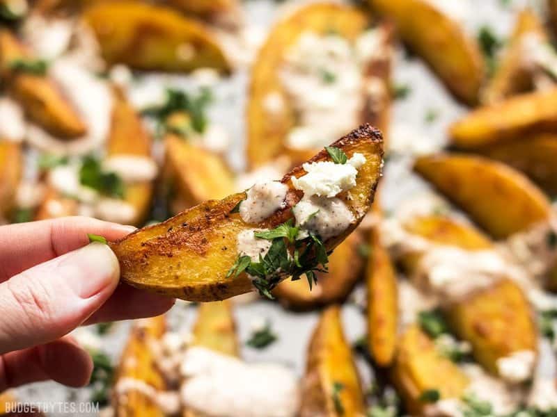 Close up of one Roasted Potato Wedge held in a hand, with the sheet pan in the background