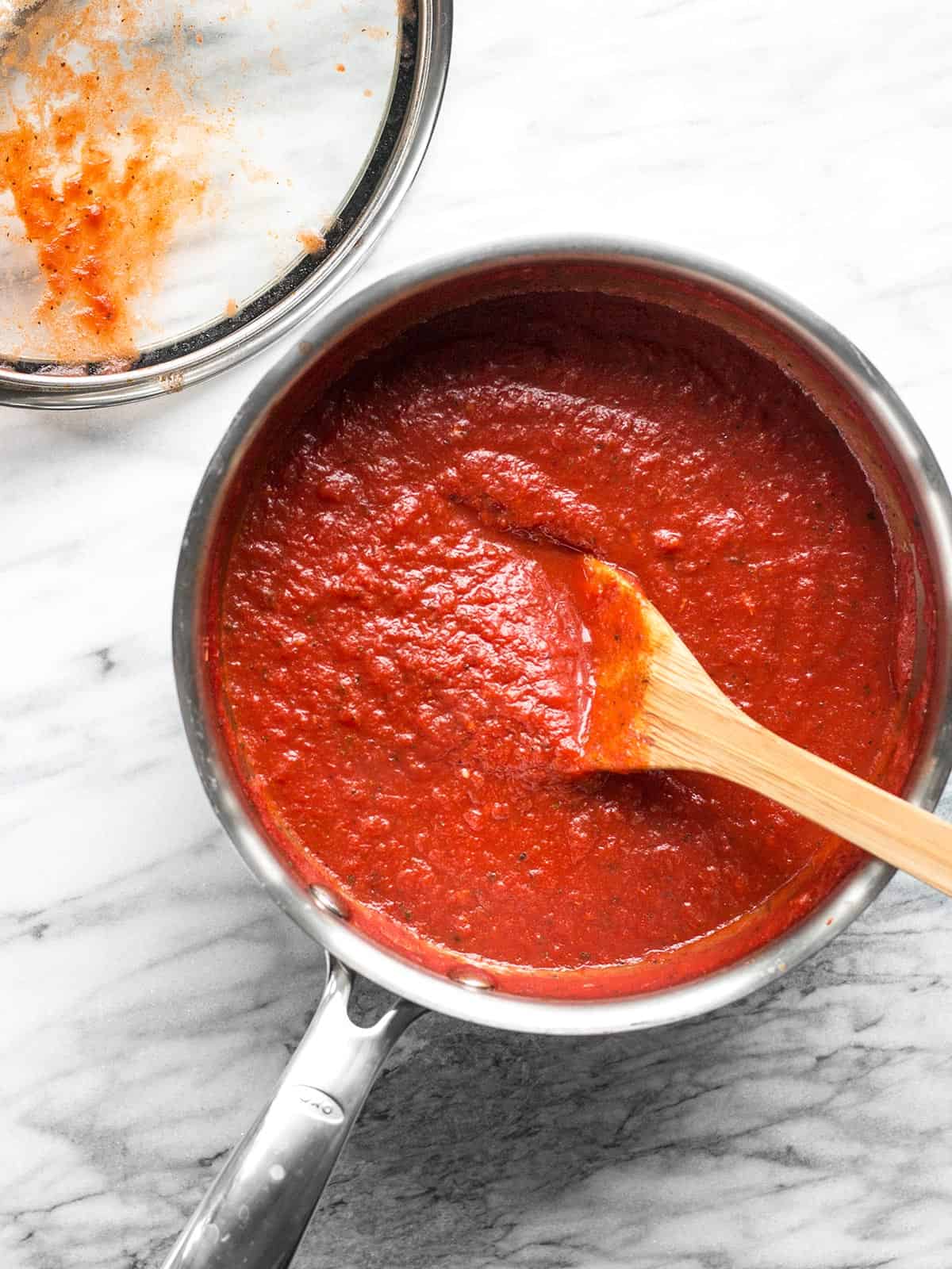 Overhead view of a sauce pot full of pizza sauce with a wooden spoon in the center.