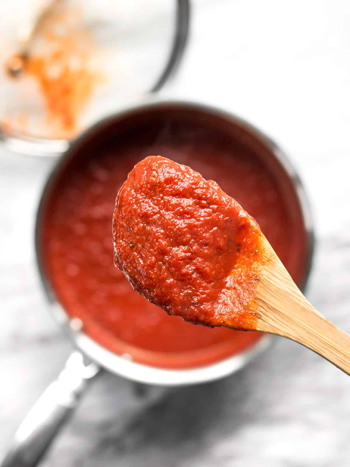 Close up of a wooden spoon full of pizza sauce held over a sauce pot.