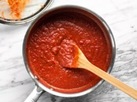 A wooden spoon in the center of a sauce pot full of homemade pizza sauce.