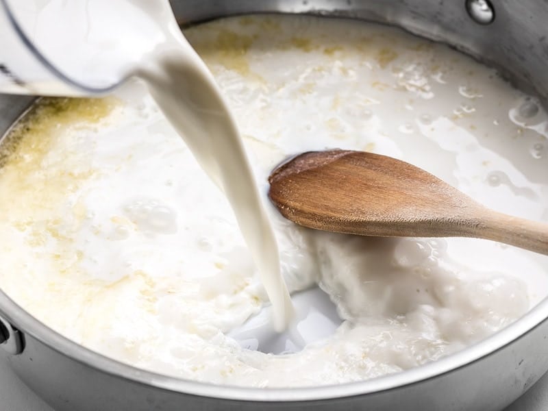 Milk being poured into butter and garlic in skillet