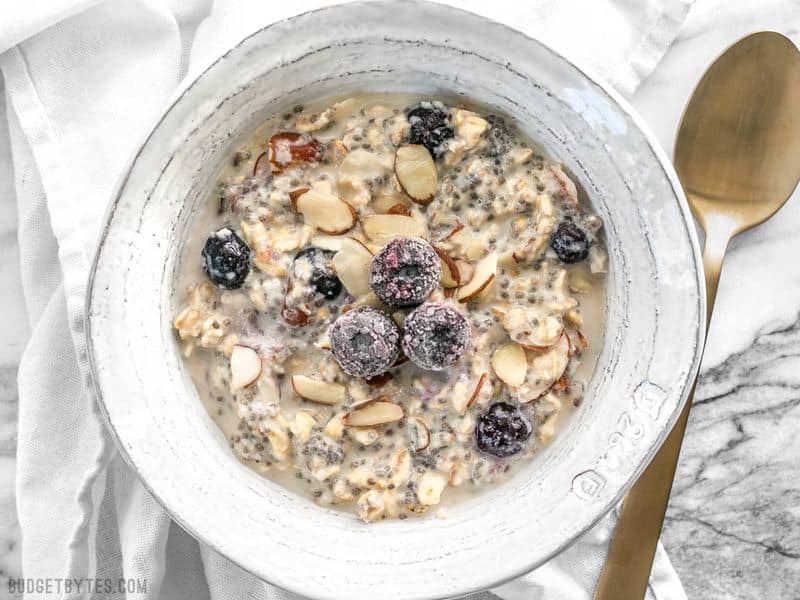 A bowl of soaked Blueberry Almond Overnight Oats with a gold spoon on the side