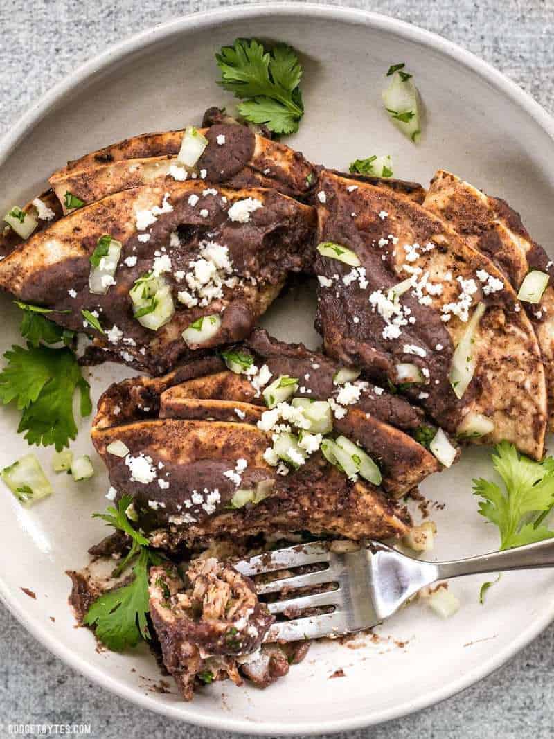 Enfrijoladas on a plate garnished with crumbled cheese and cilantro leaves. A fork ready to take a bite.