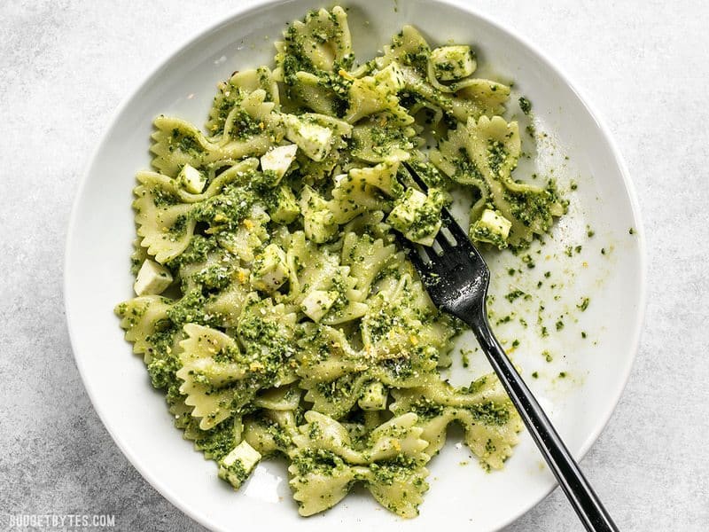 A partially eaten bowl of kale pesto pasta with mozzarella chunks