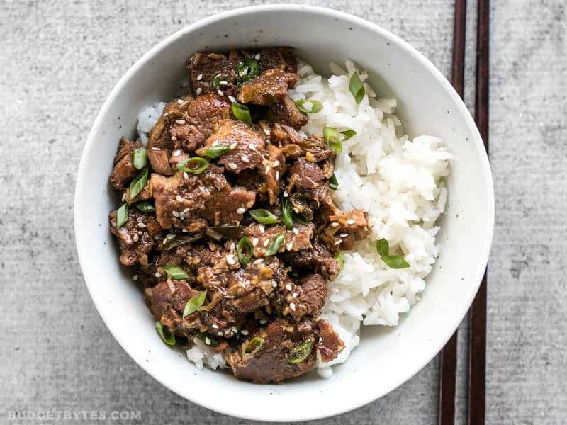 Slow Cooker Sesame Beef in a bowl with rice and green onion, chopsticks on the side