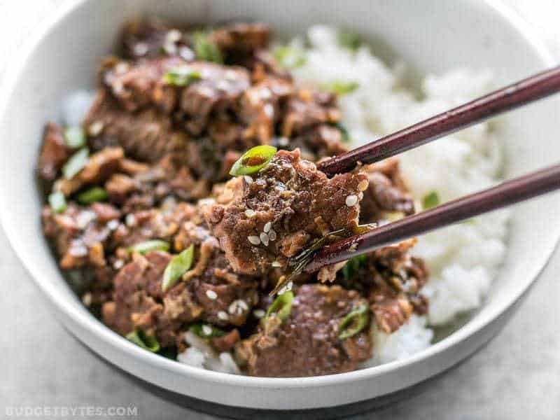 Close up of chopsticks picking up a piece of Slow Cooker Sesame Beef out of the bowl